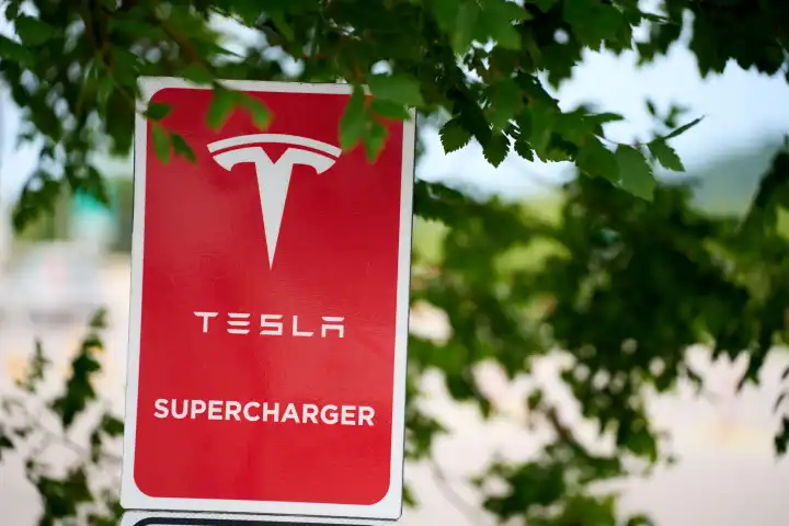 Tesla Supercharger, rotes Schild vor grünem Baum. E-Ladesäule für Tesla Elektroautos 