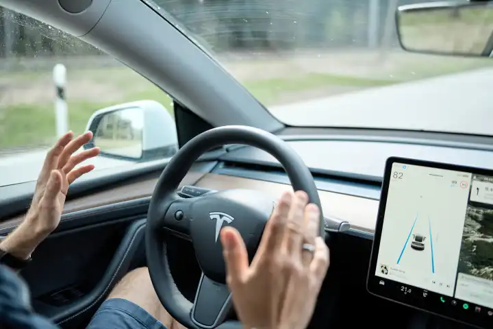 Symbolbild Autonomes Fahren, Ein Mann fährt mit einem Tesla E-Auto mit Autopilot. Er hält die Hände weg vom Lenkrad