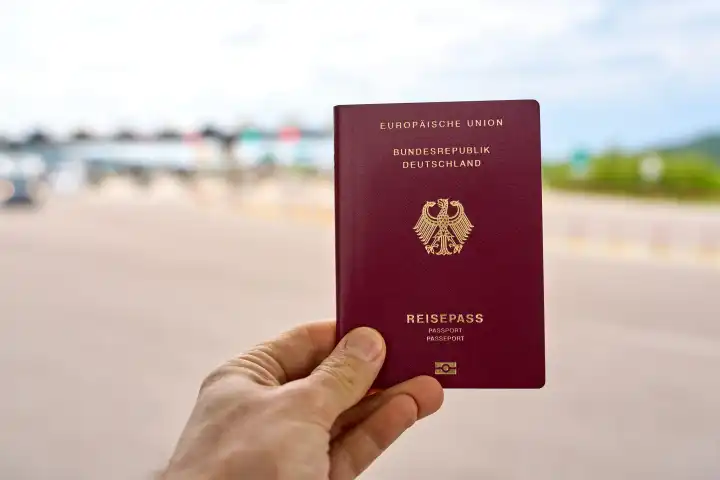 1 May 2024: Hand holding a passport of the Federal Republic of Germany in front of a border crossing. Migration and immigration concept