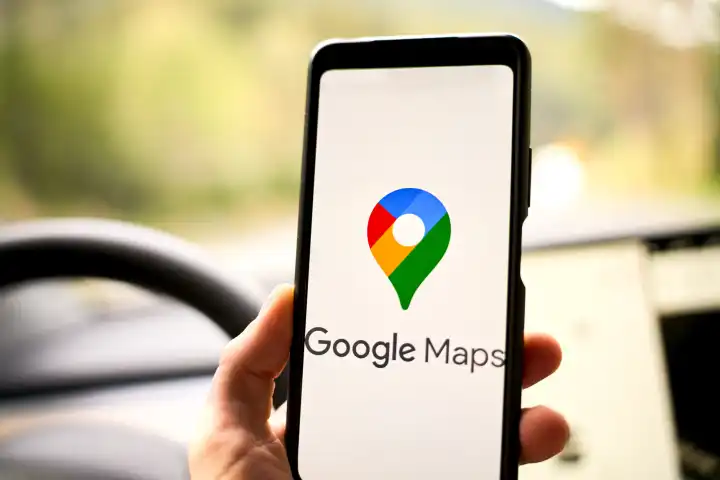 Google Maps Navigation Logo auf einem Smartphone in einem Auto vor einem Navi bzw. Navigationsgerät 