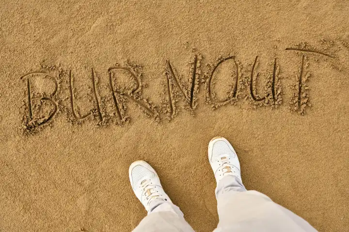 Burnout, Mann steht im Sand vor dem Schriftzug, Burnout. Mentale Gesundheit und Erschöpfung Konzept