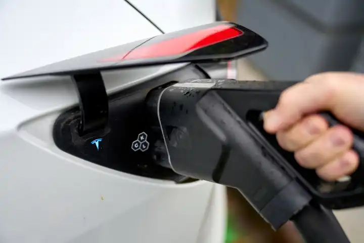 Person steckt einen Stecker bzw. Ladekabel / Ladestecker einer Ladesäule für Elektroautos in ein Elektrofahrzeug um die Batterie bzw. den Akku zu laden für die Fahrt