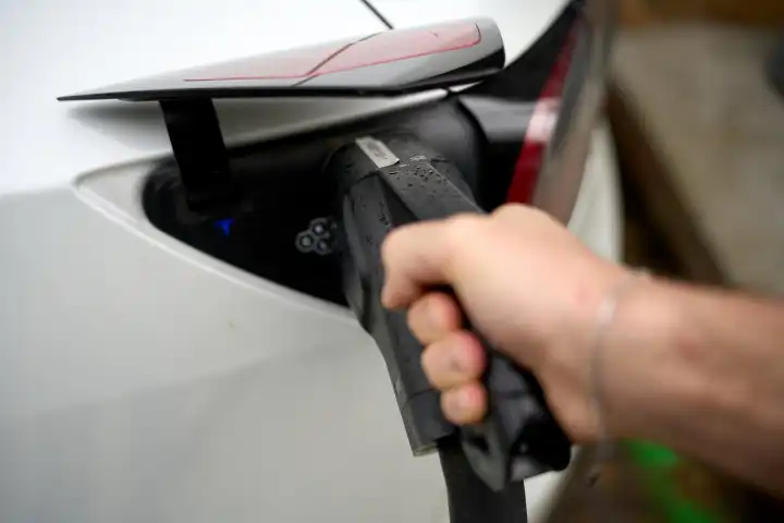  Italy - 01 May : Person inserts a plug or charging cable / charging plug of a charging station for electric cars into an electric vehicle to charge the battery for the journey