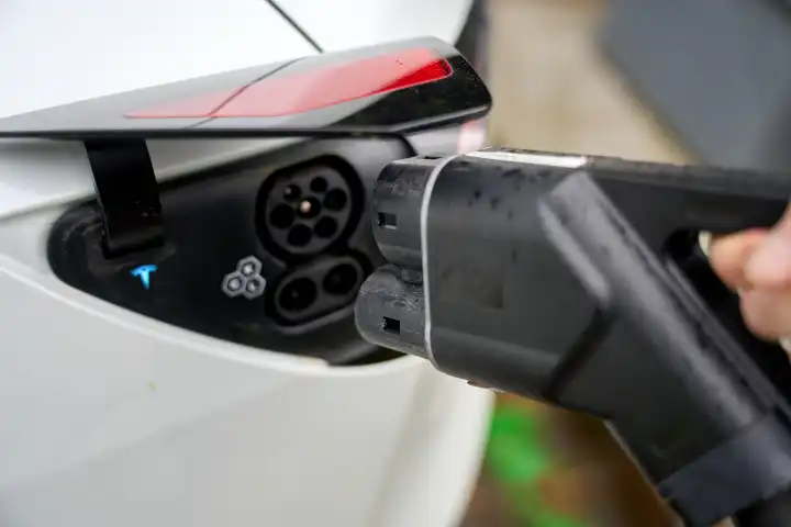 Person steckt einen Stecker bzw. Ladekabel / Ladestecker einer Ladesäule für Elektroautos in ein Elektrofahrzeug um die Batterie bzw. den Akku zu laden für die Fahrt