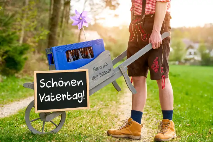 7 May 2024: Man in Bavarian lederhosen pushes a handcart on Father's Day with a sign and the greeting: Have a nice Father's Day! PHOTOMONTAGE