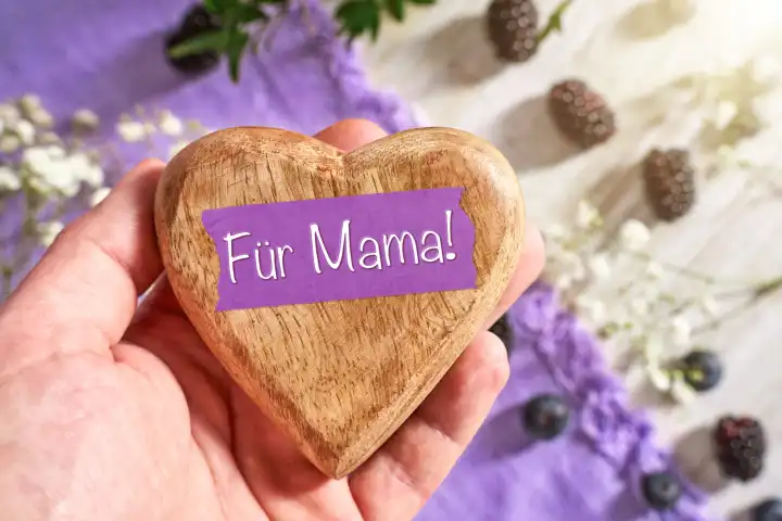 Hand hält ein Herz als Geschenk zum Muttertag mit Aufschrift: Für Mama! FOTOMONTAGE 