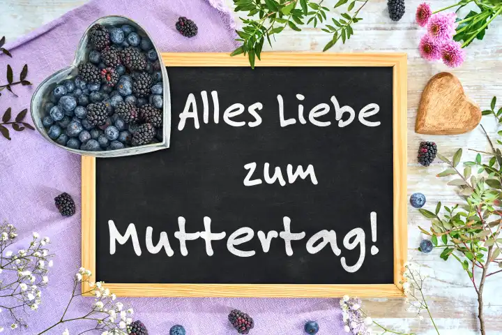 7 May 2024: All the best for Mother's Day! Greeting on a blackboard surrounded by purple decoration and blueberries. PHOTOMONTAGE