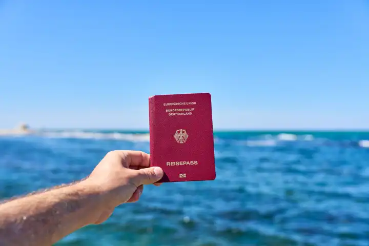 Tourist hält Reisepass der Bundesrepublik Deutschland vor das Meer im Urlaub. Einreise und Passkontrolle Konzept