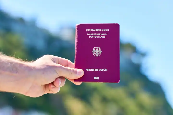Tourist hält Reisepass der Bundesrepublik Deutschland vor das Meer im Urlaub. Einreise und Passkontrolle Konzept