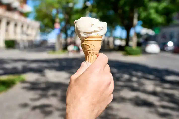Hand hält ein Eis in einer Waffel an einem sonnigen Sommertag