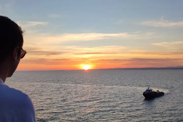 Mann mit Sonnenbrille blickt den Sonnenuntergang auf das weite Meer im Sommerurlaub, um sich vom Stress zu erholen - Konzept mentale Gesundheit