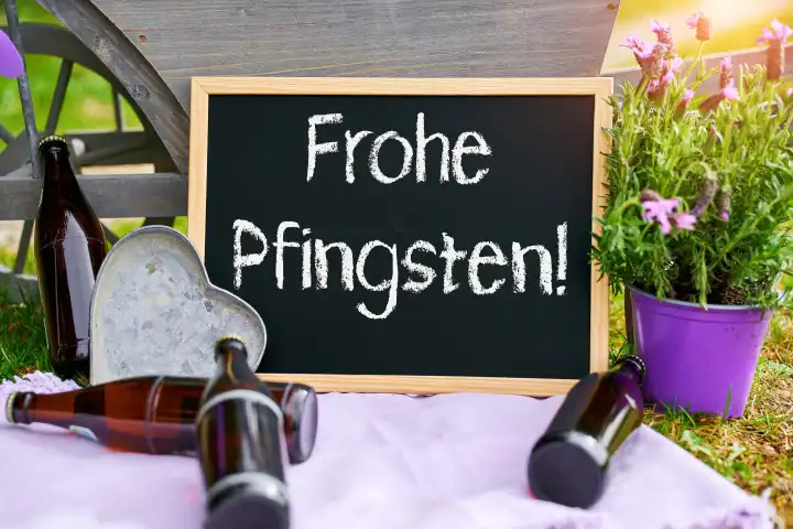 Frohe Pfingsten - Tafel im Garten mit lila Blumen und Bier. FOTOMONTAGE