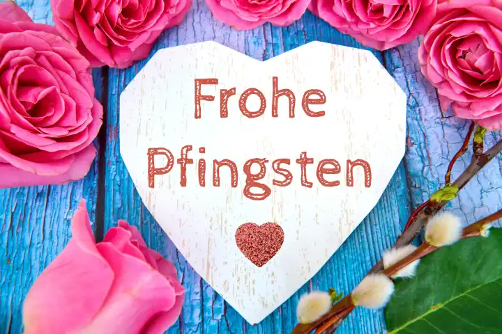 Herz aus Holz umgeben von rosa Rosen mit dem Text: Frohe Pfingsten. FOTOMONTAGE