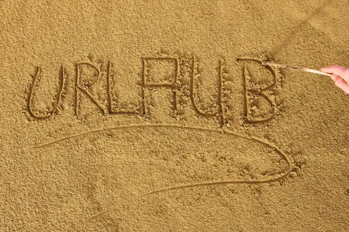 Hand schreibt mit einem Stock das Wort: Urlaub, in den Sand am Strand 