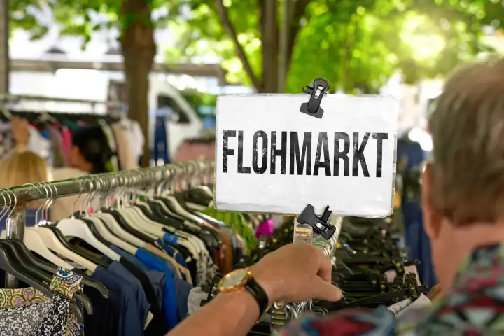 Schild: Flohmarkt, über einem Kleiderständer an dem ein Mann gebrauchte Waren anschaut. FOTOMONTAGE