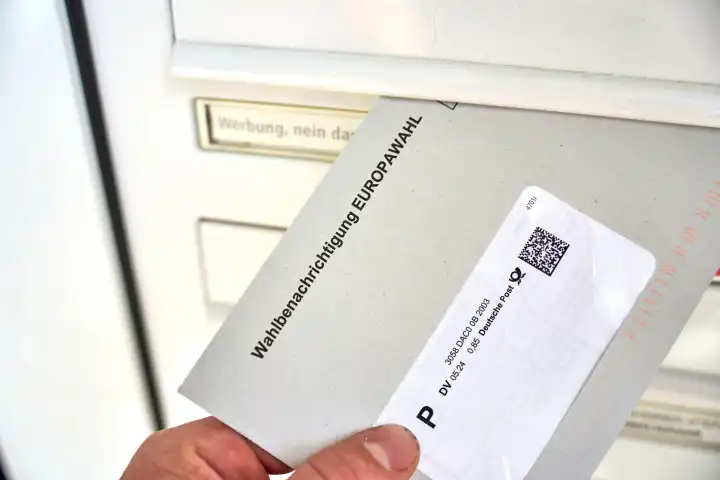 Hand holt einen Brief mit der Wahlbenachrichtigung zur Europawahl 2024 aus dem Briefkasten