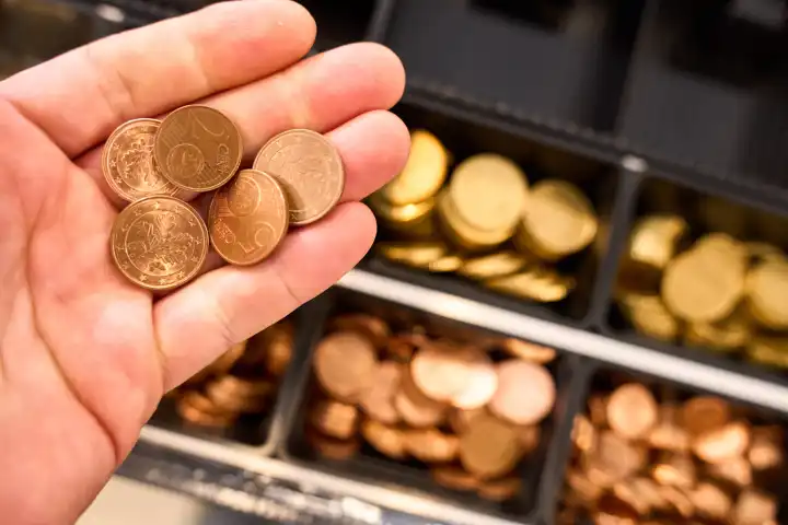 Hand hält Euro Cent Kleingeld Münzen, Wechselgeld vor eine Kasse in einem Geschäft 