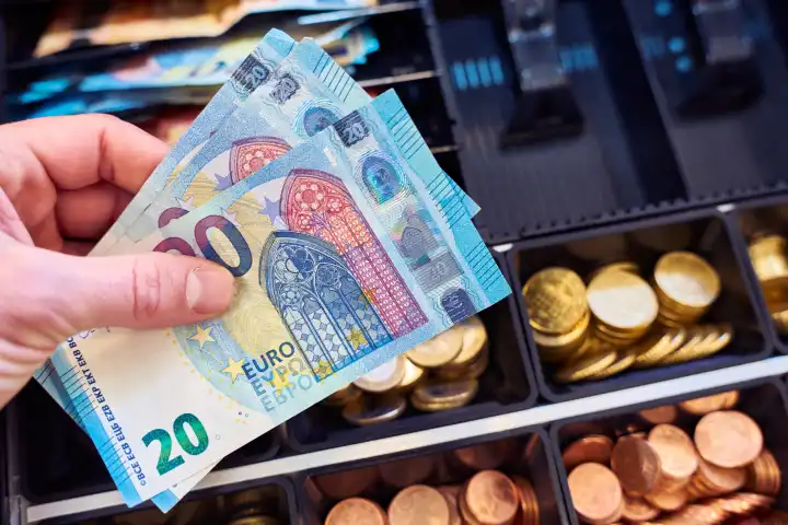 Hand hält mehrere 20 Euro Bargeld, Geldscheine vor die Kasse in einem Geschäft. Handel und Wirtschaft Konzept