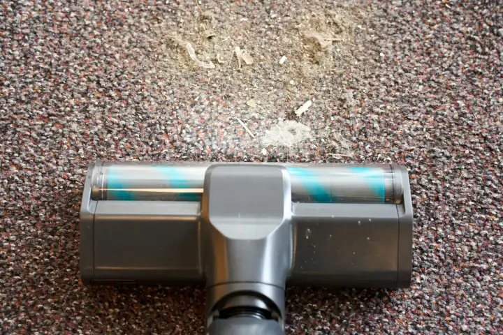 Staubsauger befreit einen Teppich im Haushalt von Staub und Dreck mit einer Bodendüse