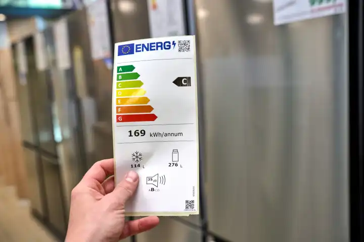 Eine Hand hält ein Energie Label der Europäischen Union in einem Geschäft mit Haushaltsgeräten wie Kühlschränke