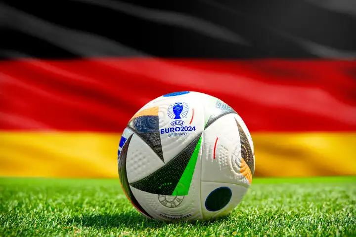 Fußball Europameisterschaft UEFA EURO 2024 in Deutschland: Offizieller Spielball von Adidas auf dem Spielfeld mit Nationalflagge von Deutschland. FOTOMONTAGE