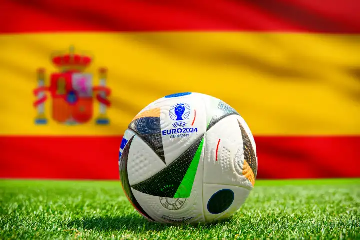 Fußball Europameisterschaft UEFA EURO 2024 in Deutschland: Offizieller Spielball von Adidas auf dem Spielfeld mit Nationalflagge von Spanien. FOTOMONTAGE