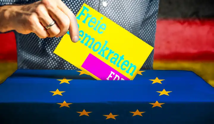 Themenbild Europawahl 2024 in Deutschland: Mann wirft einen Stimmzettel in eine Wahlurne mit Flagge der Europäischen Union. Stimmabgabe für die Partei: FDP Freie Demokraten. FOTOMONTAGE