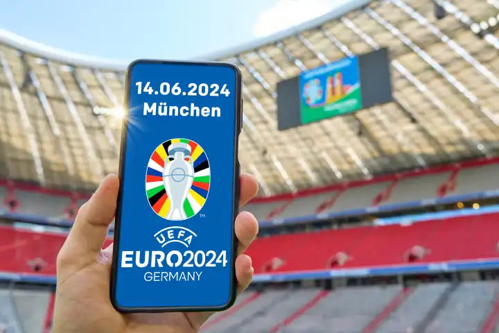 Symbolbild Eröffnungsspiel der Fußball EM 2024 in der Allianz Arena in München, Deutschland gegen Schottland am 14.06.2024. Eine Hand hält ein Smartphone mit UEFA EURO 2024 Logo im Fußballstadion. FOTOMONTAGE