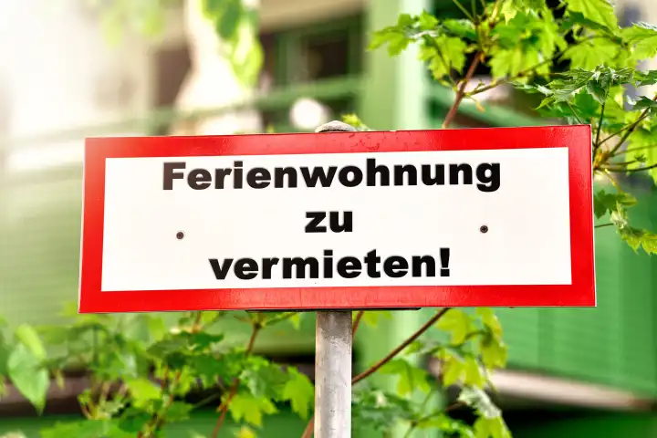 Ferienwohnung zu vermieten! Schriftzug auf einem Schild bei Sonnenschein vor einem Haus. FOTOMONTAGE