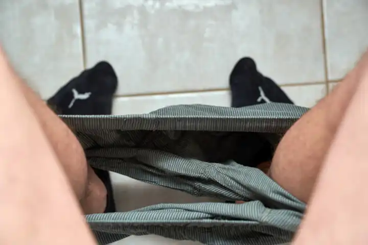 Mann sitzt mit heruntergezogener Unterhose auf der Toilettenschüssel und hat Stuhlgang, bzw. macht sein Geschäft auf dem WC