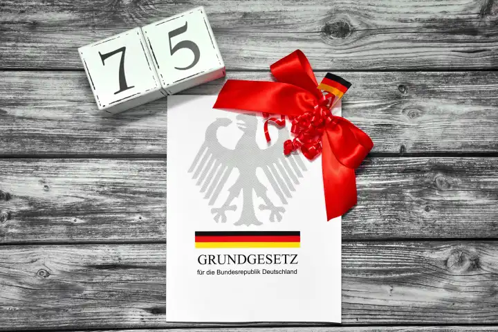 Das Grundgesetz der Bundesrepublik Deutschland wird 75 Jahre alt. Das Grundgesetz Buch mit einer roten Schleife und Datum Würfel mit der Zahl 75