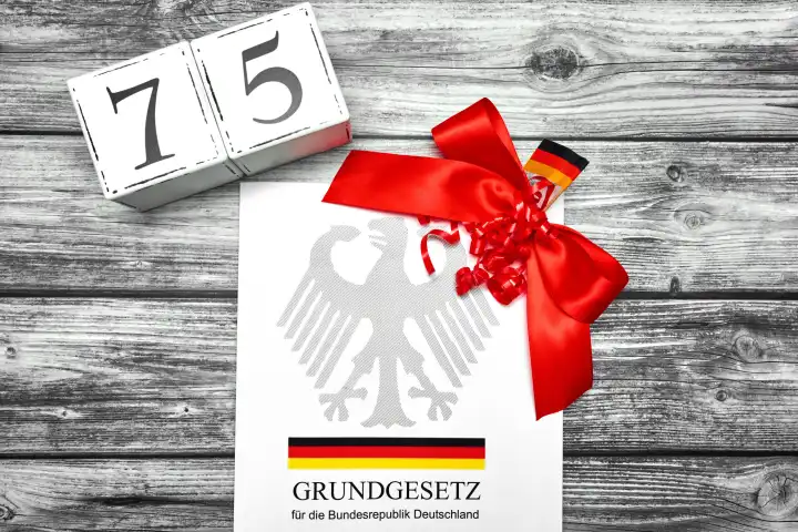 Das Grundgesetz der Bundesrepublik Deutschland wird 75 Jahre alt. Das Grundgesetz Buch mit einer roten Schleife und Datum Würfel mit der Zahl 75
