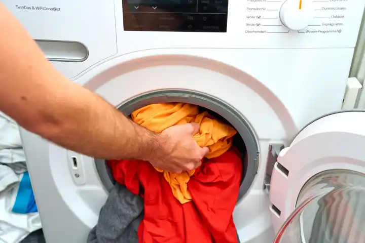 Wäsche waschen, Konzept, richtige Haushaltsführung. Hand belädt das Bullauge einer Waschmaschine mit schmutziger bzw. getragener Kleidung