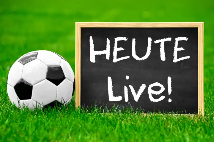 Fußball Heute Live! Symbolbild, Ein Fußball auf einem Sportplatz neben einem Schild mit Aufschrift: Heute Live! FOTOMONTAGE