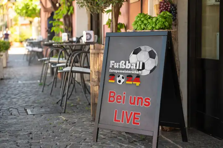 Bei uns Live! Schriftzug mit Deutschlandflagge auf einem Schild vor einem Gastronomiebetrieb. Symbolbild Public Viewing der Fußball Europameisterschaft 2024. FOTOMONTAGE