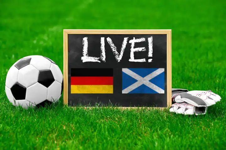 Fußball Europameisterschaft 2024 Themenbild: Live-Übertragung des Spiels Deutschland gegen Schottland  Konzept. Ein Fußball mit einer Tafel und Handschuhen auf dem Spielfeld mit Aufschrift: Live! FOTOMONTAGE