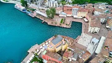  Malerische Altstadt von Riva del Garda mit ihren historischen Gebäuden und charmanten Gassen, die sich um die Piazza III Novembre und den markanten Torre Apponale versammeln. Die Uferpromenade mit ihren einladenden Cafés und Restaurants lädt Touristen zum Verweilen und Genießen der wunderschönen Seelandschaft ein. 