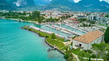 Riva del Garda, Lake Garda, Italy - June 25, 2024: Small harbor of Riva del Garda with sailboats and sailing ships and view from Lake Garda to the buildings of the city