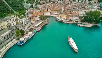 Navigazione Lago di Garda Fähre, bzw. Schiff im Hafen vom historischen Riva del Garda am Gardasee, zwischen traditionellen Gebäuden und Restaurants.