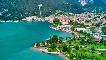 Weiter Blick mit der Drohne von der Gemeinde Torbole hin zu Riva del Garda am Gardasee über blauem, klarem Wasser. Schöne Strände und einladende Wanderwege laden zum Baden und Spazieren ein.