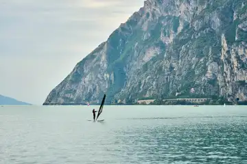 Windsurfer genießen das ruhige Wasser und die malerische Landschaft in Torbole am Gardasee, Italien. Die Region ist ein Paradies für Wassersportler und Naturliebhaber