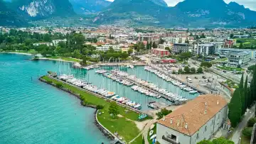 Riva del Garda, Lake Garda, Italy - June 25, 2024: Small harbor of Riva del Garda with sailboats and sailing ships and view from Lake Garda to the buildings of the city