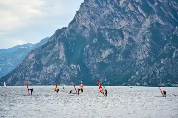 Windsurfer genießen das ruhige Wasser und die malerische Landschaft in Torbole am Gardasee, Italien. Die Region ist ein Paradies für Wassersportler und Naturliebhaber