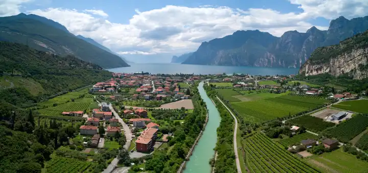 Luftaufnahme vom Gardasee in Norditalien, die das malerische Dorf Torbole zeigt, eingebettet in üppige Weinberge und die majestätischen Berge des Trentino in Italien