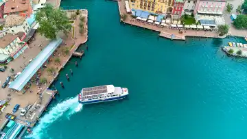 Navigazione Lago di Garda Fähre, bzw. Schiff im Hafen vom historischen Riva del Garda am Gardasee, zwischen traditionellen Gebäuden und Restaurants.
