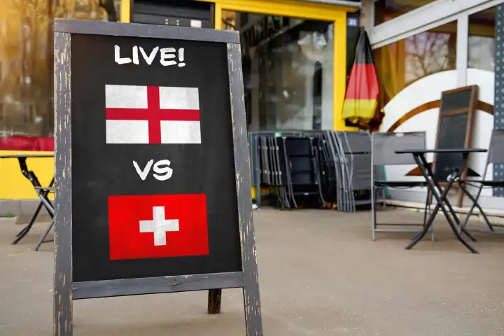 Fußball-Europameisterschaft 2024 Viertelfinale Symbolbild - Länderspiel England Schweiz. Public Viewing Konzept, eine Tafel vor einer Bar mit englischer und schweizer Flagge und dem Schriftzug LIVE! FOTOMONTAGE