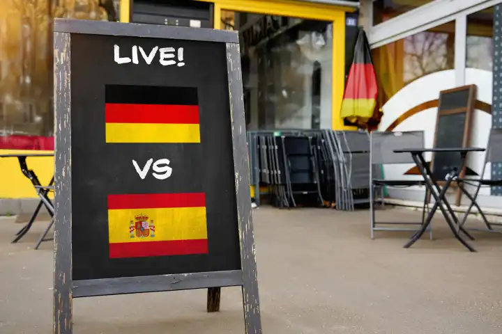 Fußball-Europameisterschaft 2024 Viertelfinale Symbolbild - Länderspiel Deutschland Spanien. Public Viewing Konzept, eine Tafel vor einer Bar mit deutscher und spanischer Flagge und dem Schriftzug LIVE! FOTOMONTAGE