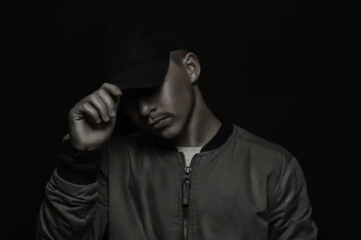 Teen Boy Holding Cap with Bomber Jacket in Front of Black Background