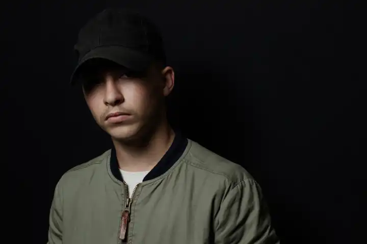 Teen Boy Posing with Black Cap and Bomber Jacket in Front of Black Background