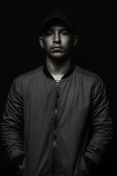 Teen Boy Posing with Black Cap and Bomber Jacket in Front of Black Background